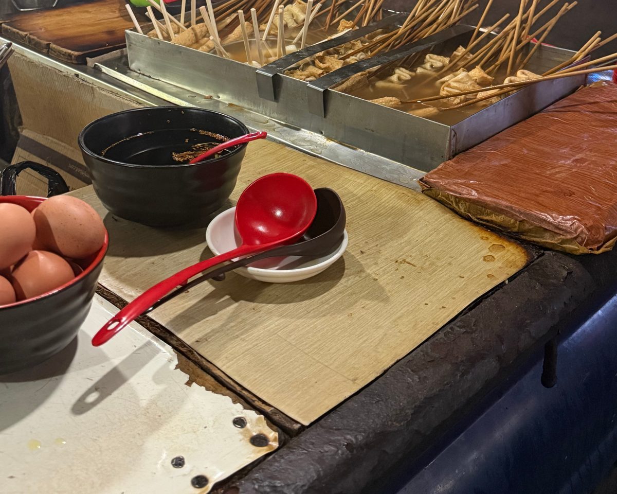 Fish cake skewers standing in broth trays on the truck counter, with a bowl, a ladle, and eggs in front