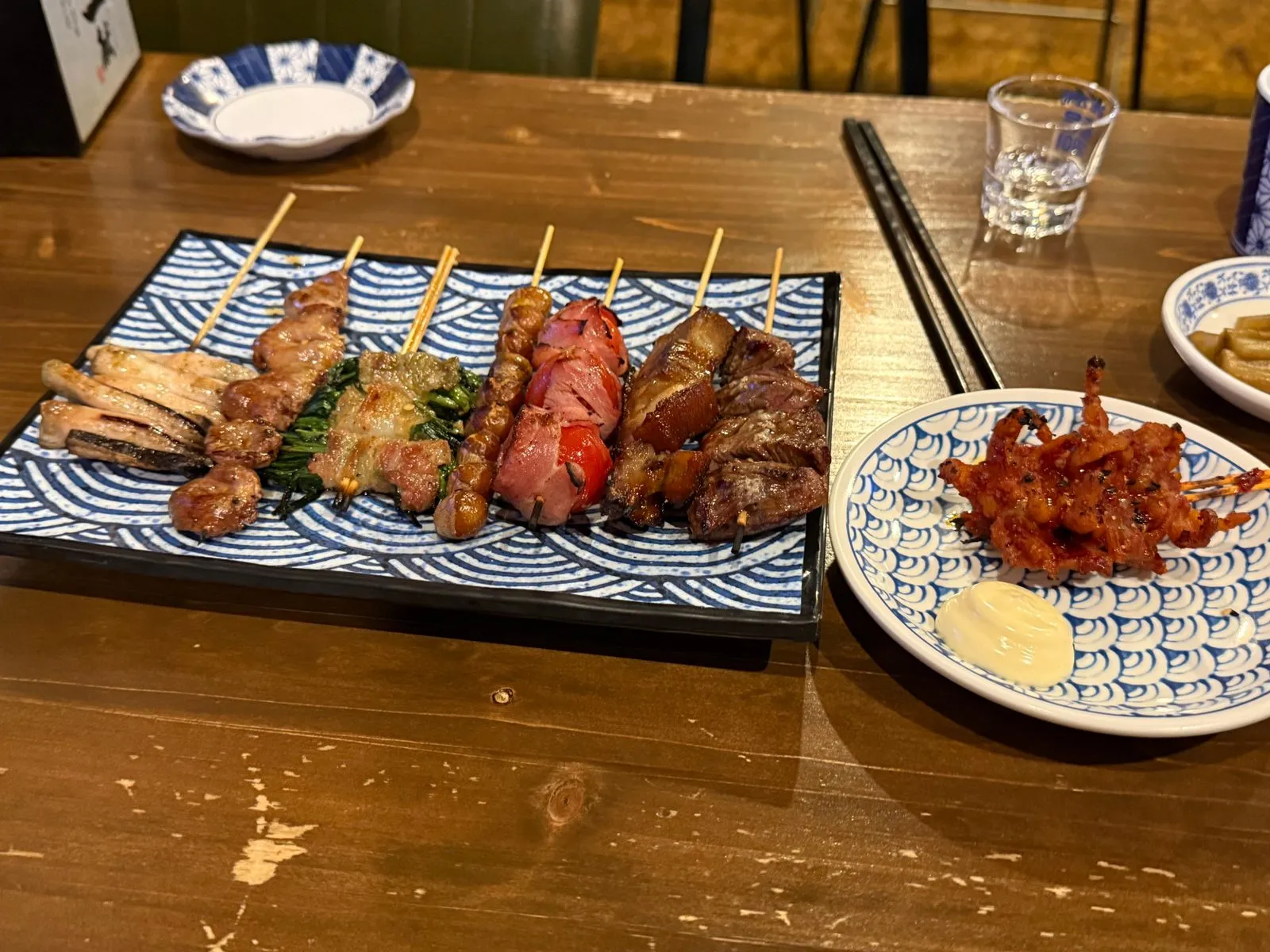 파란 물결무늬 접시에 나란히 놓인 여러 가지 꼬치와 작은 접시에 담긴 양념 꼬치