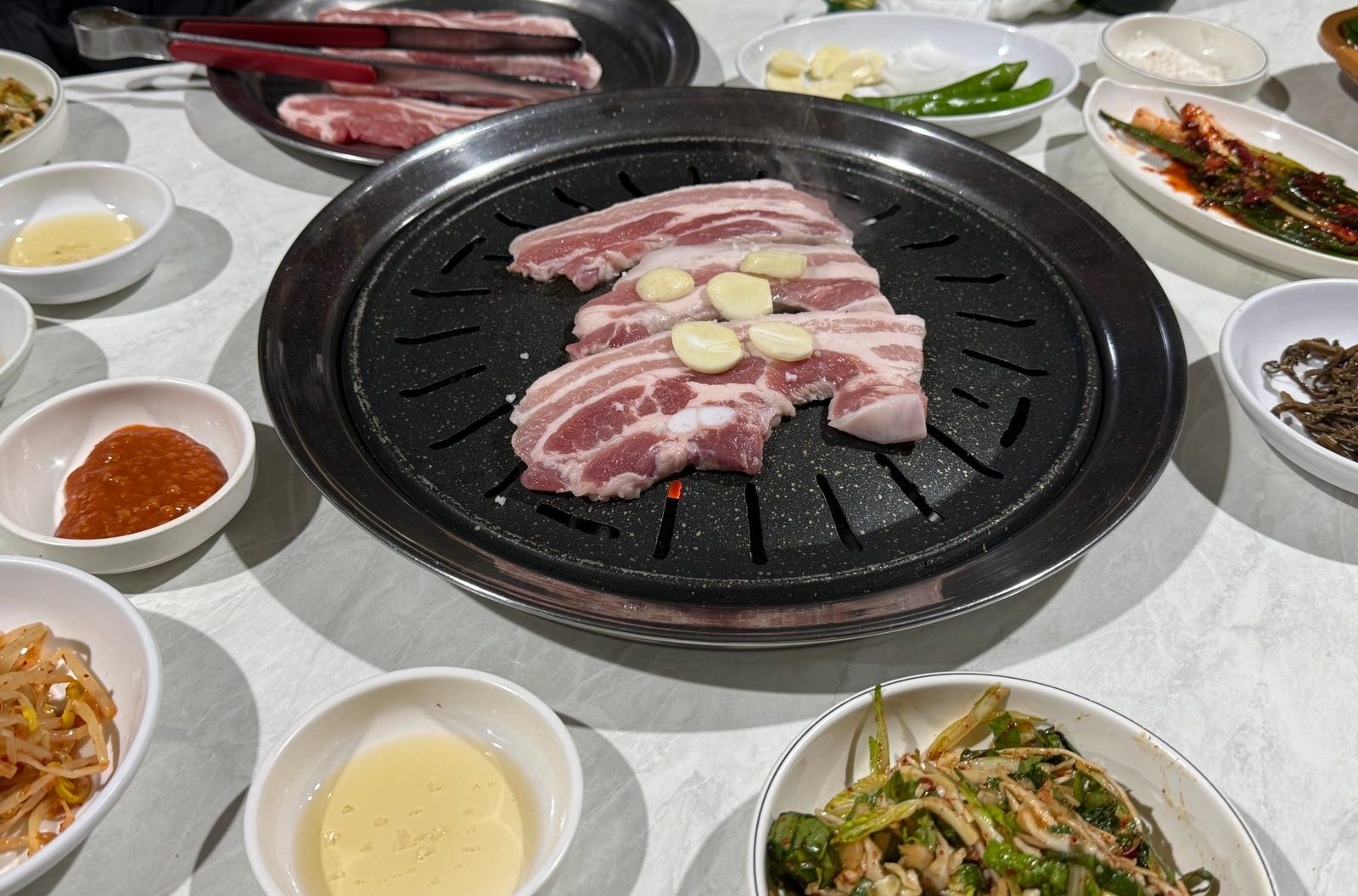 검은 불판 위에 올린 생삼겹살과 주변에 놓인 밑반찬