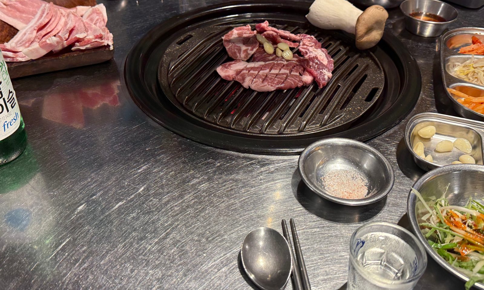 Meat cooking on a round grill plate, with side dishes placed around it