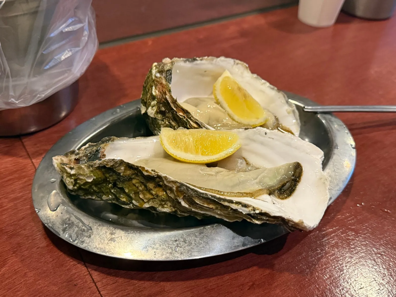 Two large oysters on a silver plate, each topped with a slice of lemon