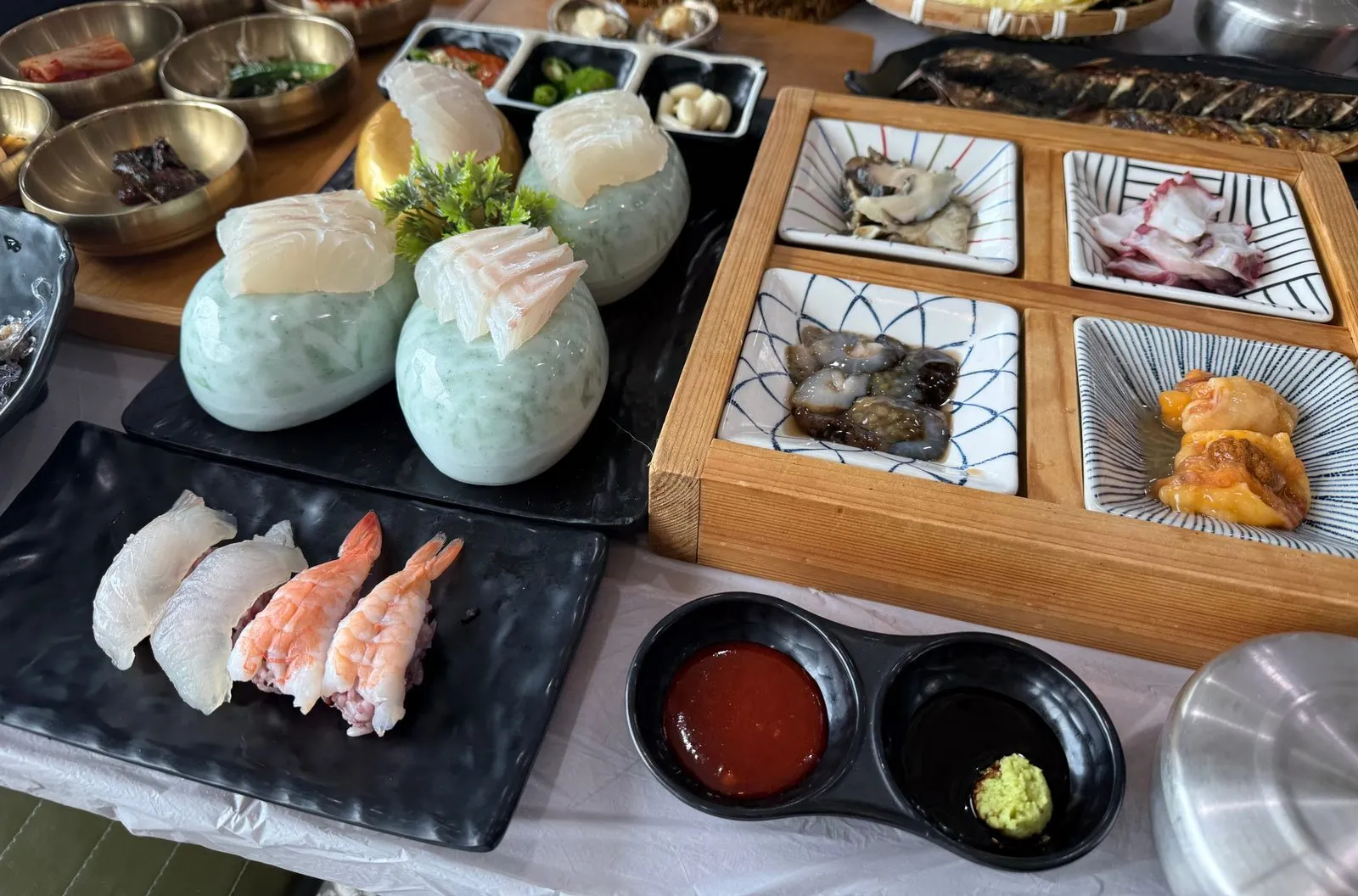 A table with a plate of sushi, round bowls, and seafood in a wooden box divided into four