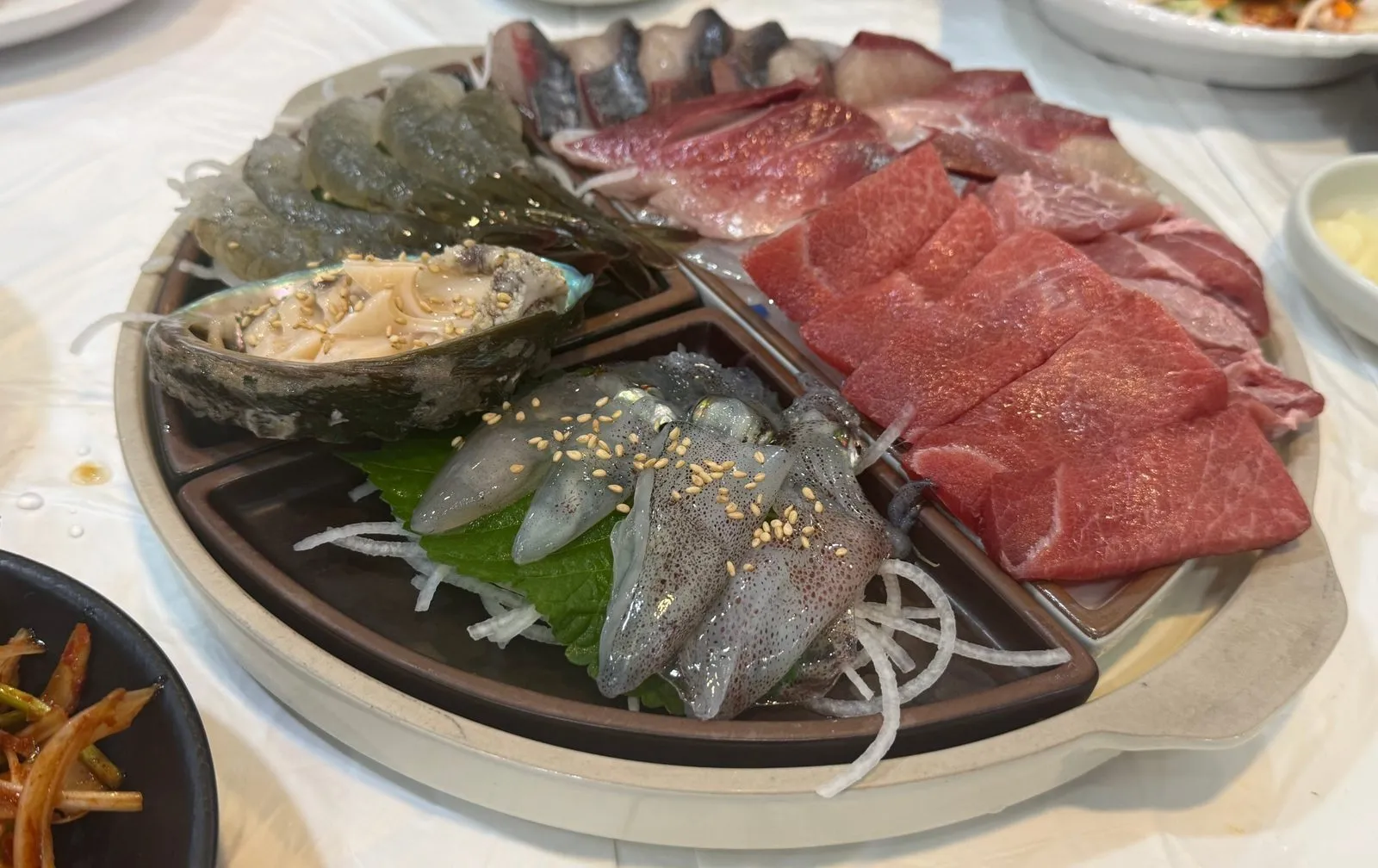 A divided plate with red tuna, shrimp, abalone, and other seafood