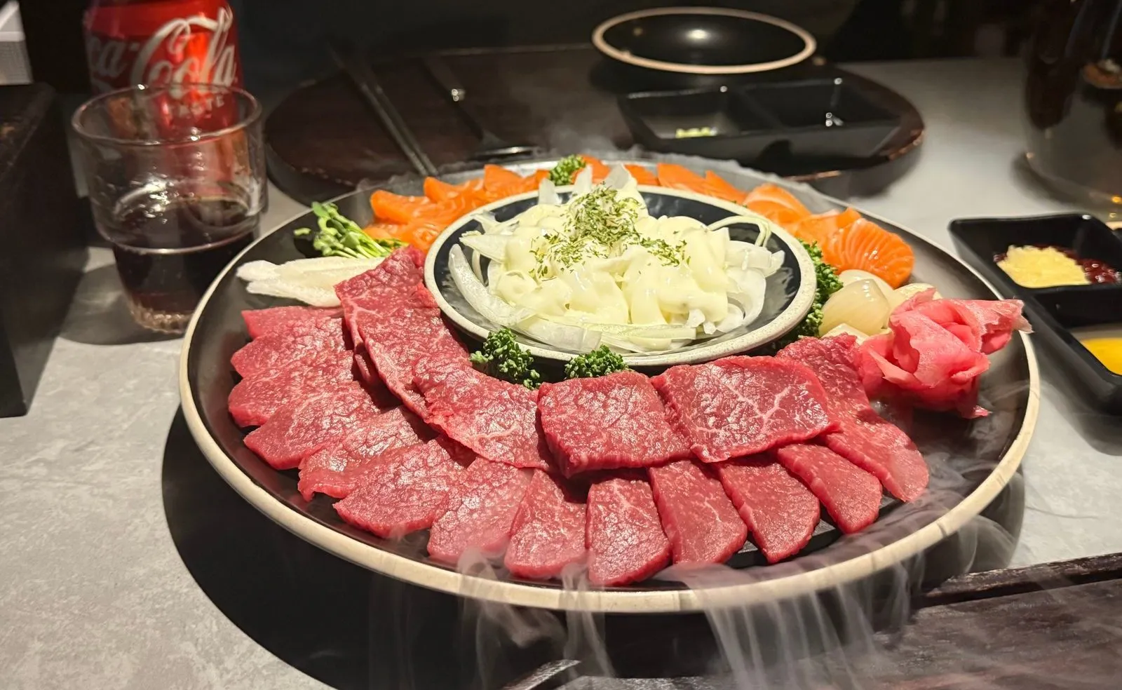 Raw beef and salmon sashimi on a round plate, with white mist spreading below it