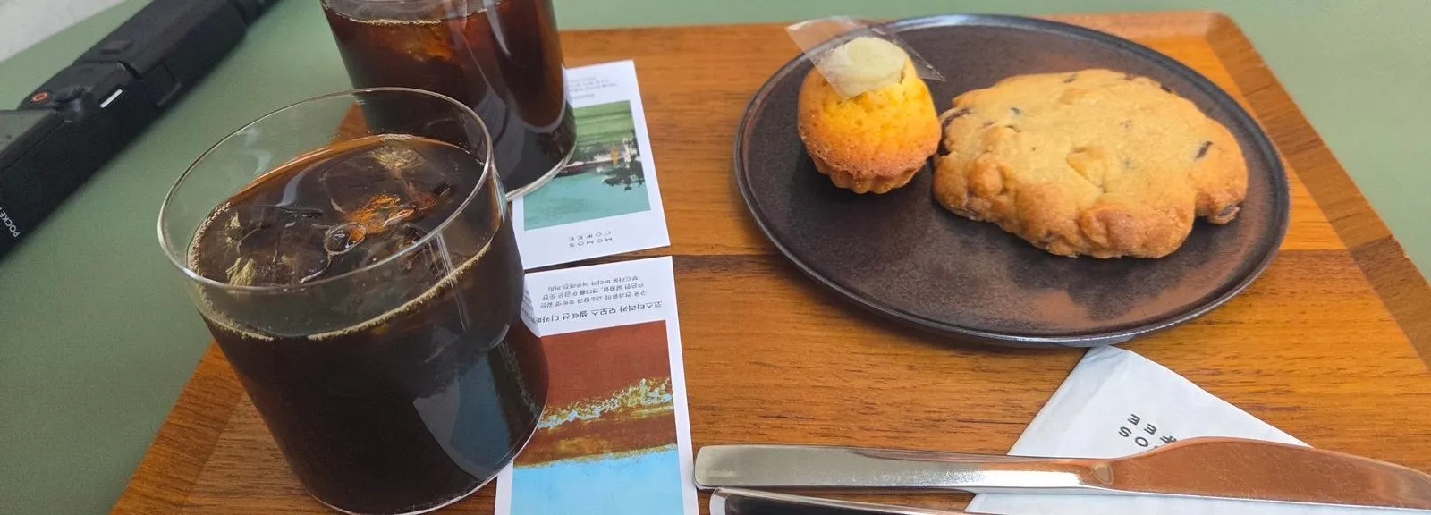 Two iced coffees on a tray with a madeleine and a cookie on a plate