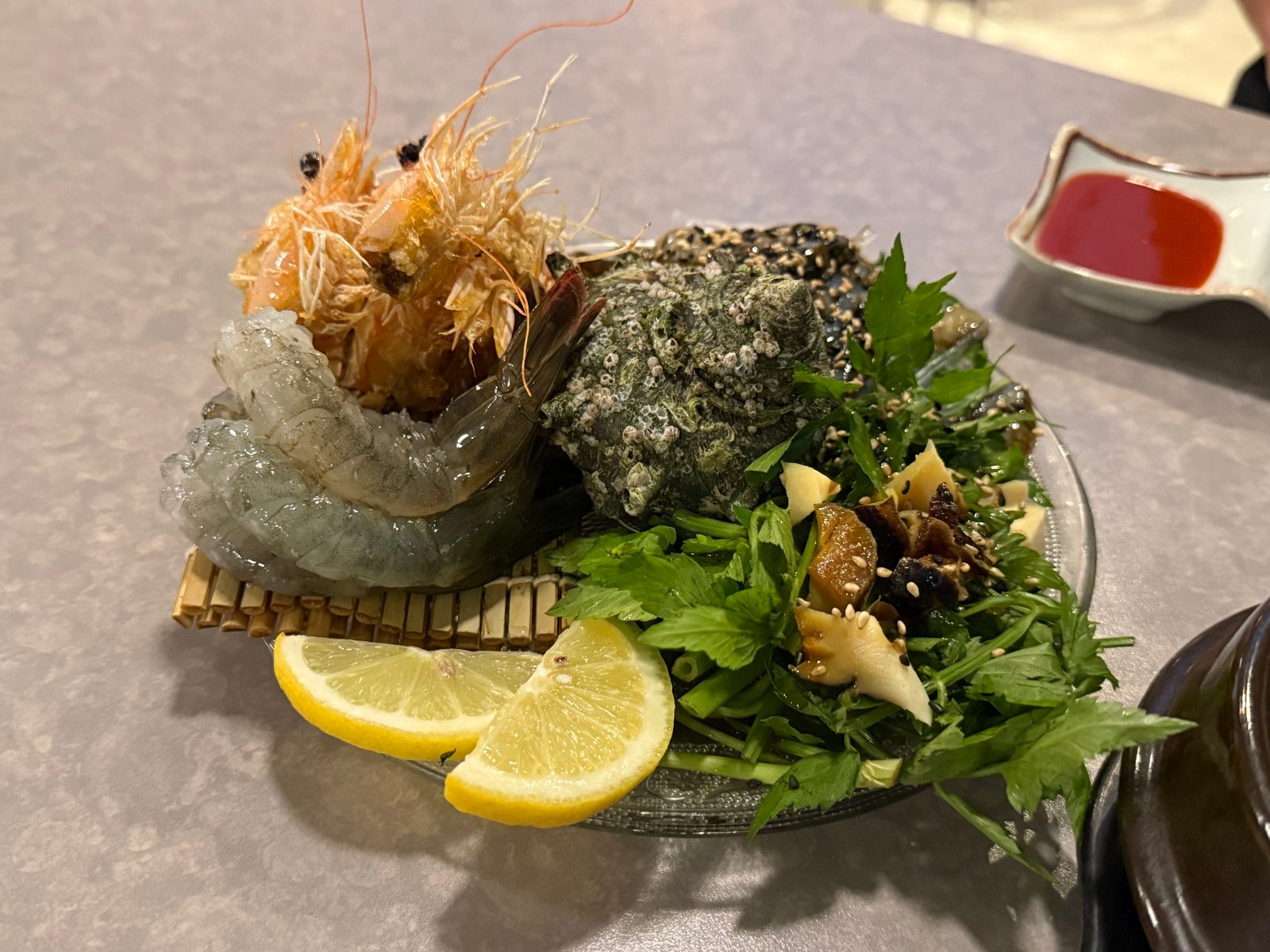 Raw shrimp and other seafood on a plate with greens and lemon wedges