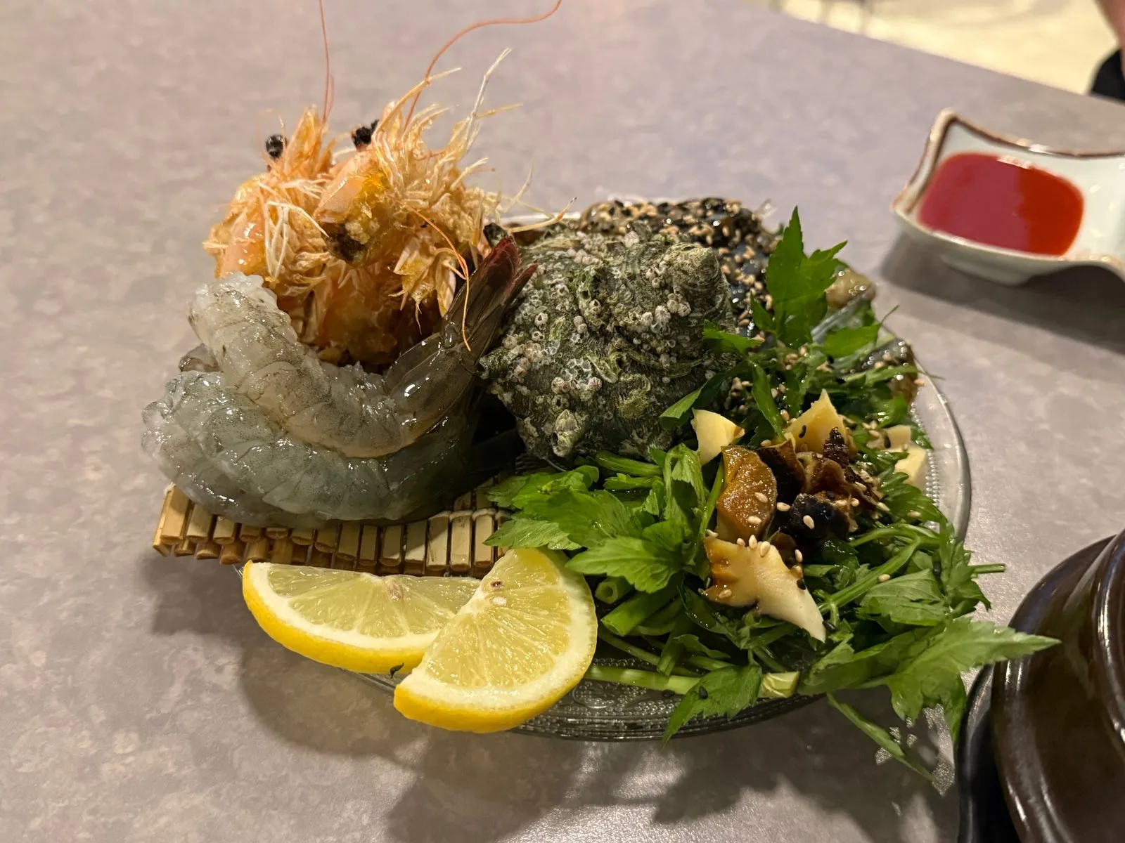 Raw shrimp and other seafood on a plate with greens and lemon wedges