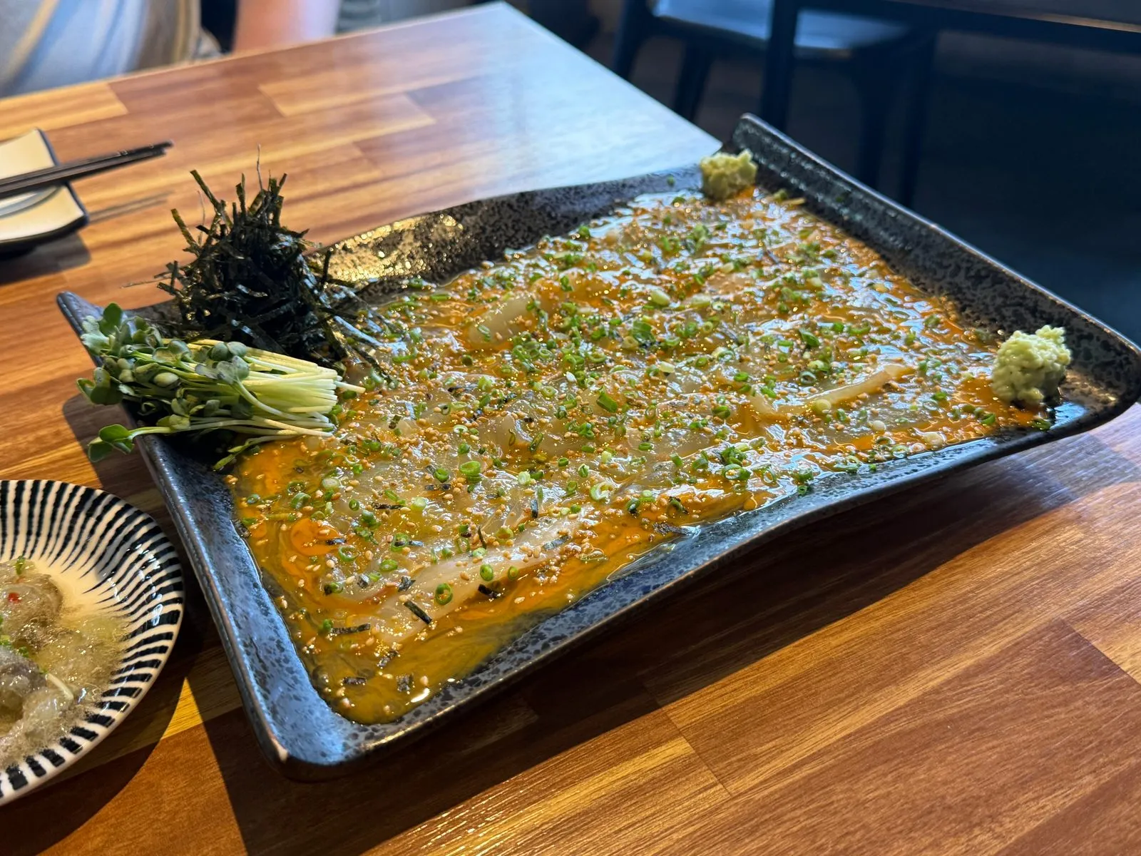 Flounder sashimi covered with sea cucumber innards sauce on a black rectangular plate, with seaweed on one side