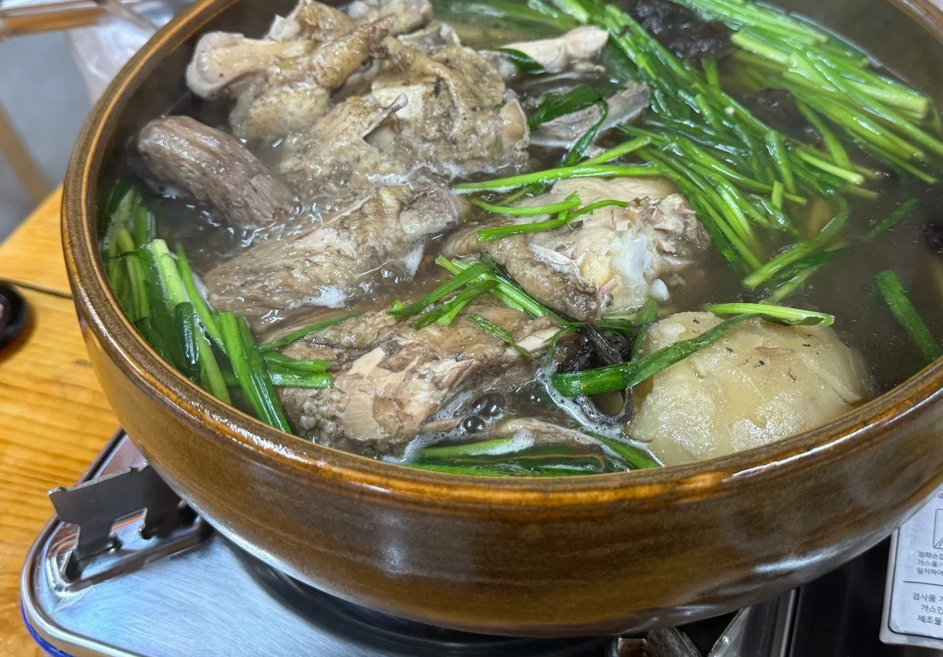 뚝배기 냄비에서 끓고 있는 토종닭백숙과 그 위에 얹은 부추와 능이버섯
