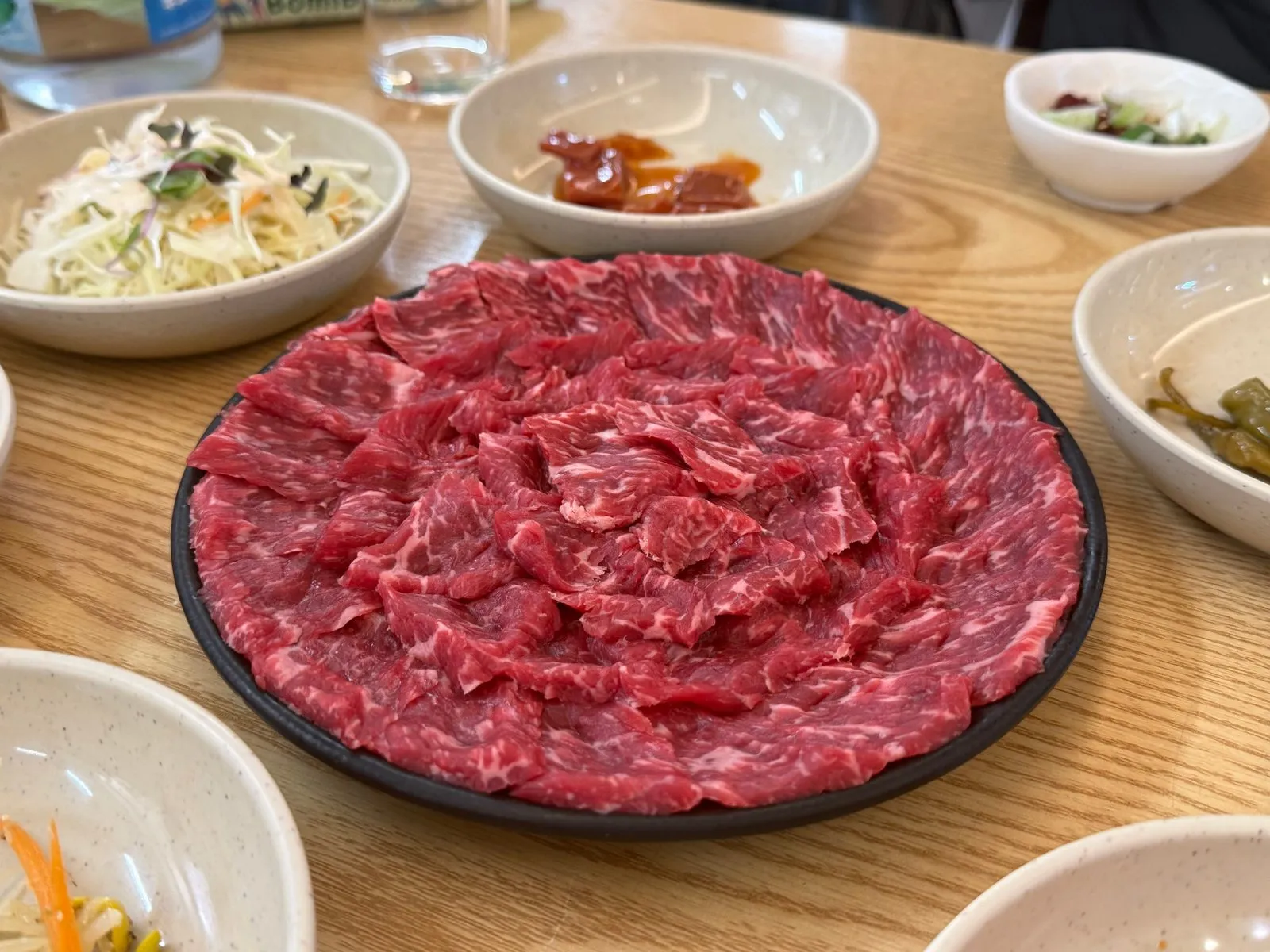 Red raw beef spread out on a black plate, surrounded by side dishes