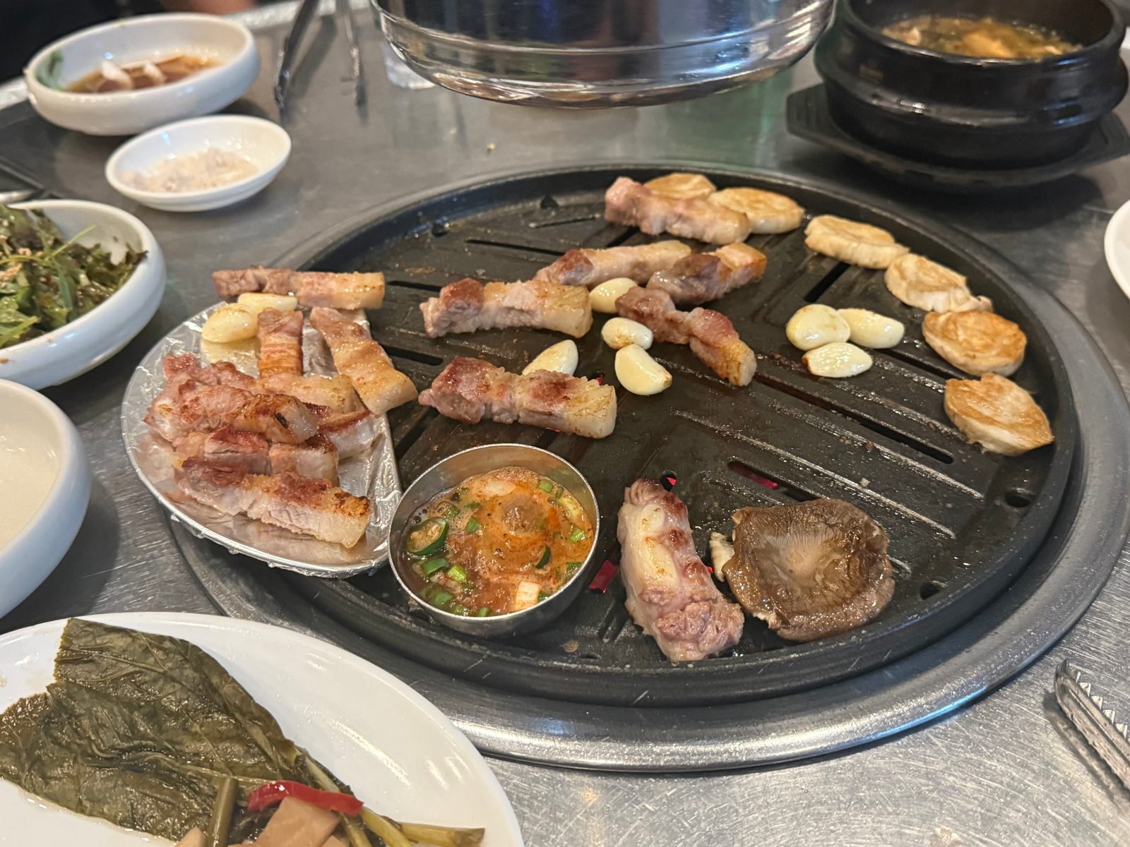 Pork belly and garlic cooking on a round grill plate, with side dishes beside it