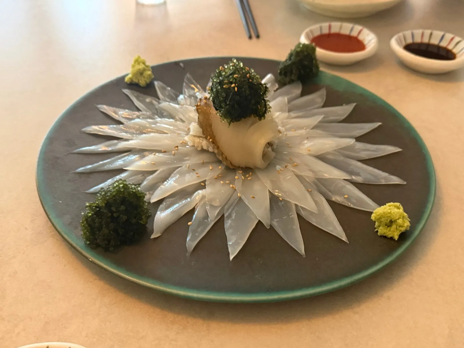 Raw bigfin reef squid spread out like petals in a circle, with green seaweed