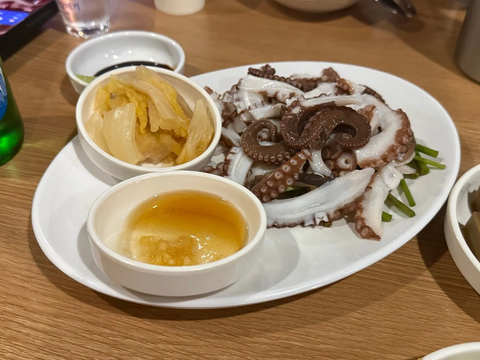 Boiled octopus on a white plate with two small bowls of sauce