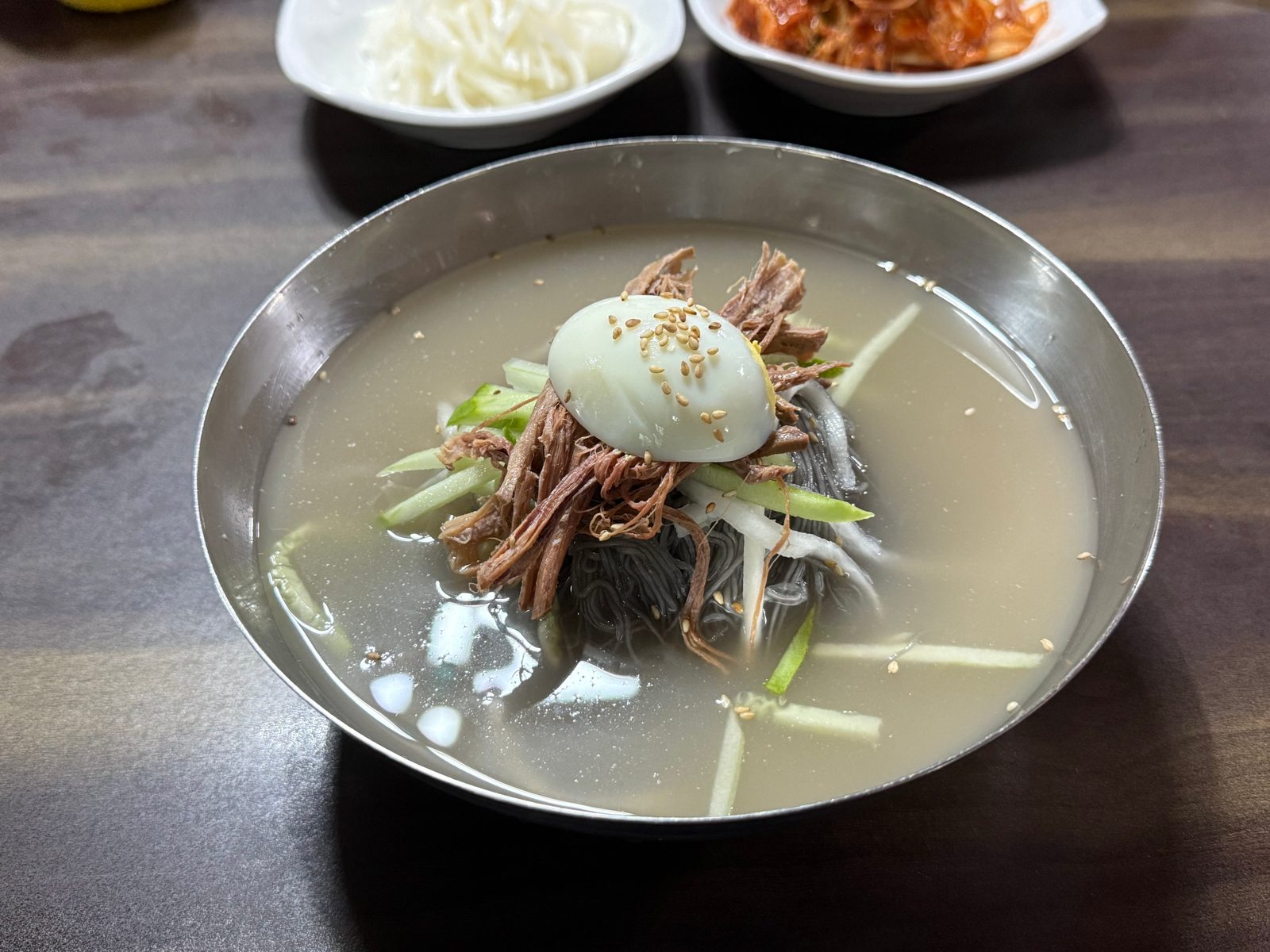 Cold noodles in broth in a metal bowl, topped with a boiled egg and garnishes