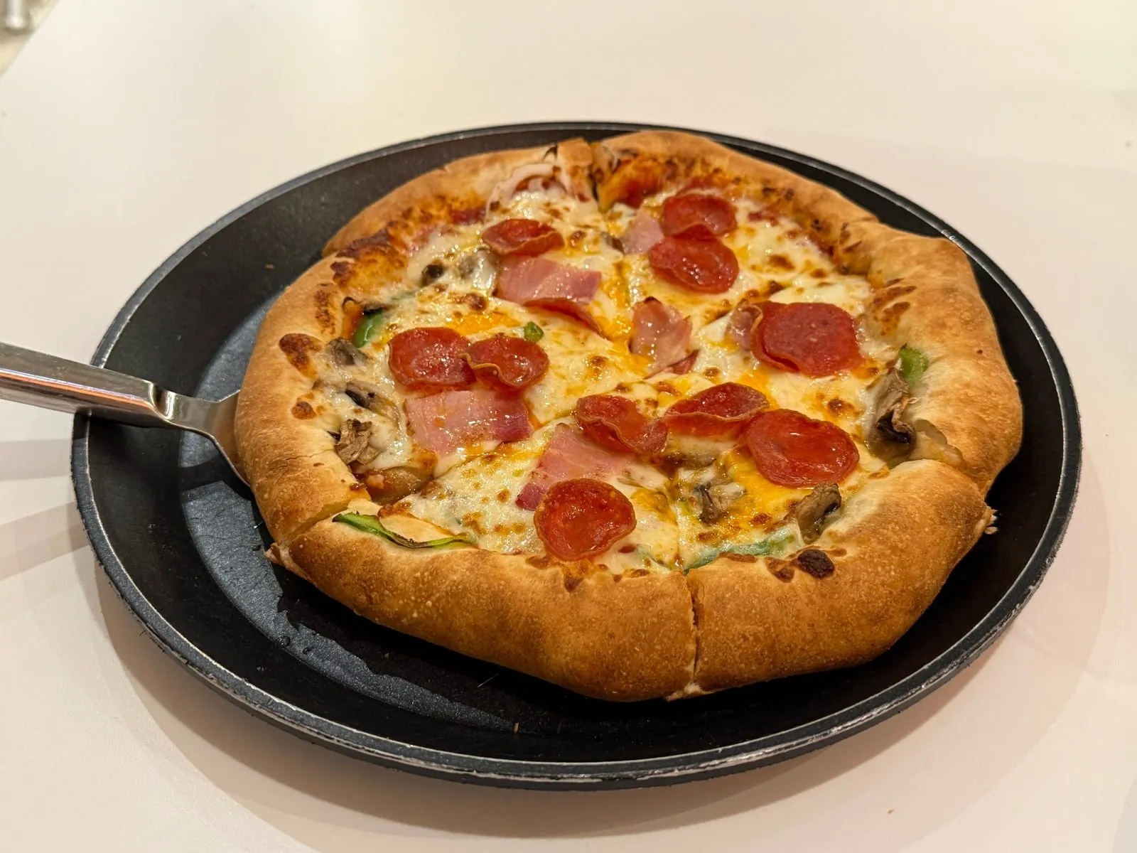A whole pizza topped with pepperoni and ham in a black pan