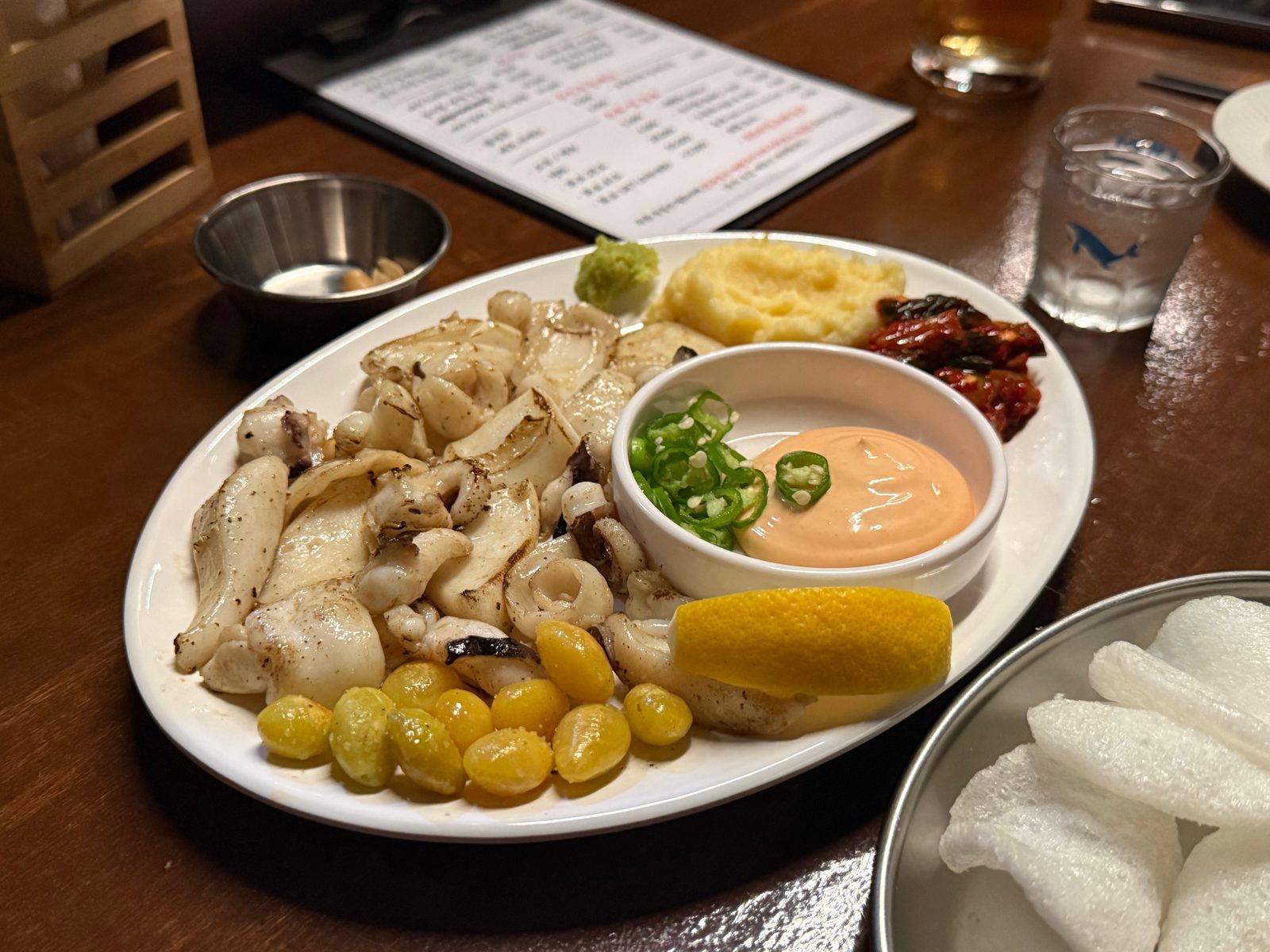 Grilled cuttlefish and ginkgo nuts on a white plate with a bowl of sauce in the middle