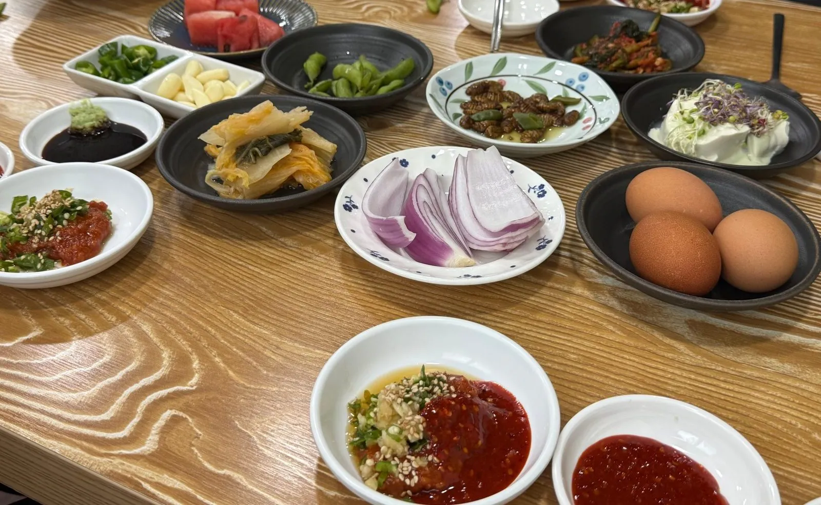 나무 무늬 상 위에 놓인 여러 가지 밑반찬과 양념장