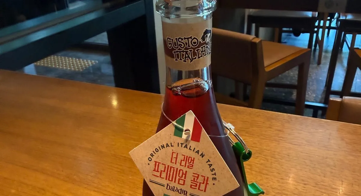 A glass bottle of cola with a name tag and a green bottle opener on its neck