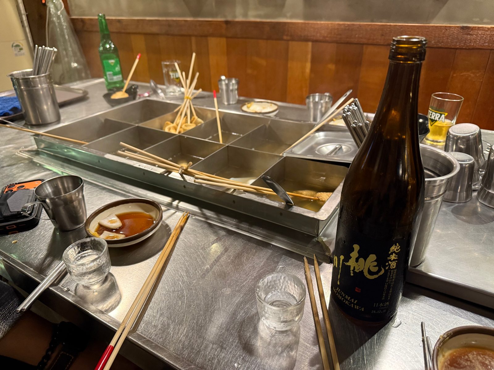 A sectioned oden broth tray with a black sake bottle in front of it