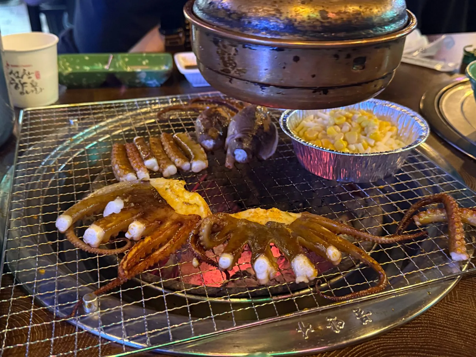 숯불 석쇠 위에서 익고 있는 낙지와 은박 그릇에 담긴 옥수수