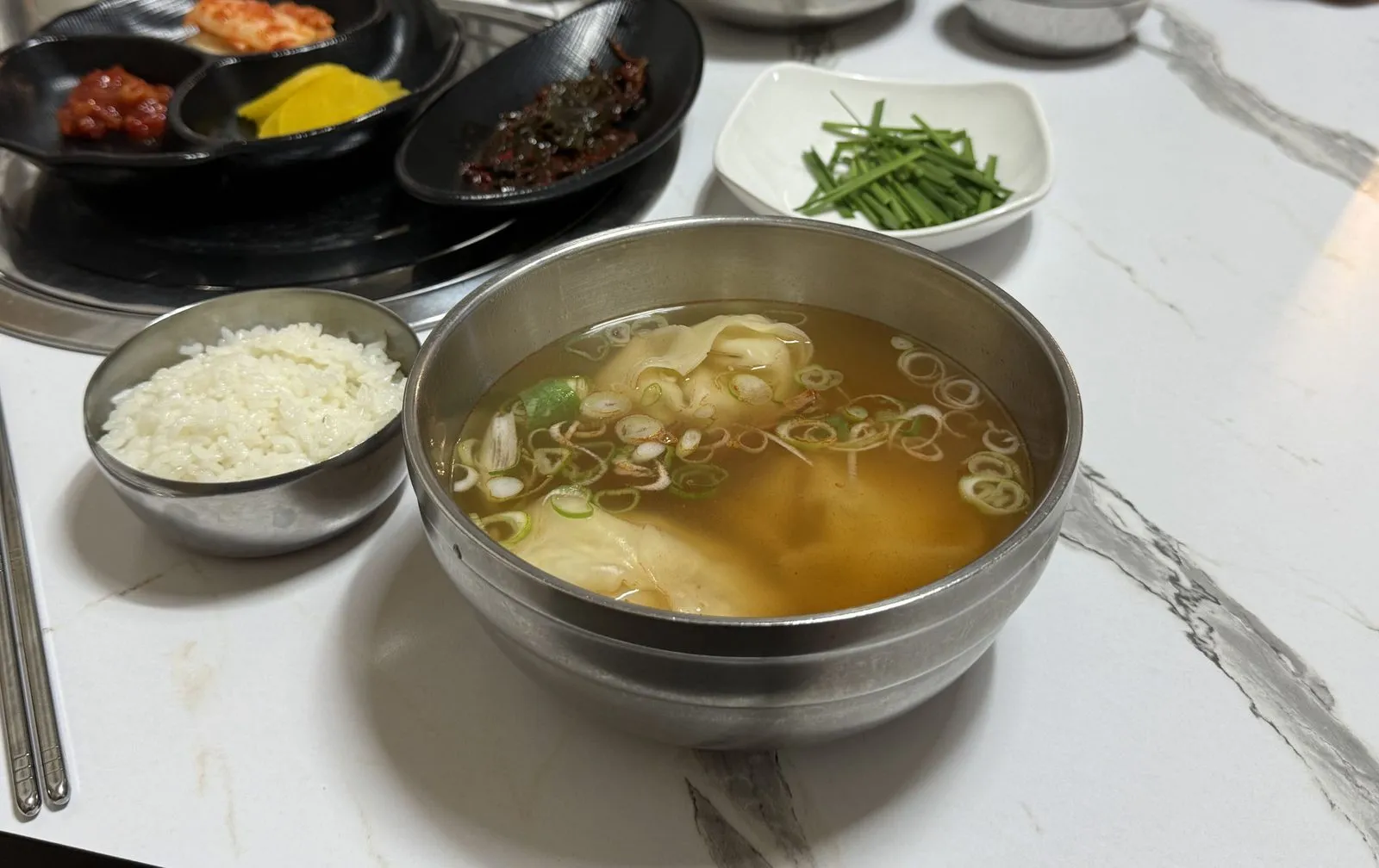 만둣국 한 그릇과 공깃밥, 부추와 김치 등 반찬이 놓인 상차림