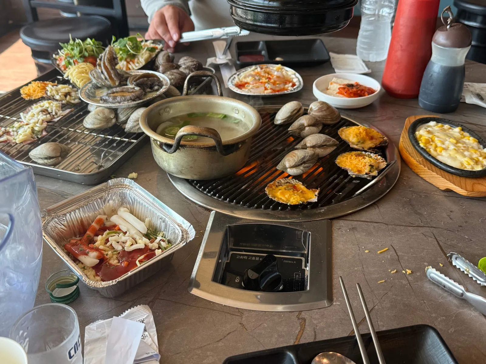 A table with two grills covered with clams, scallops, and cheese dishes