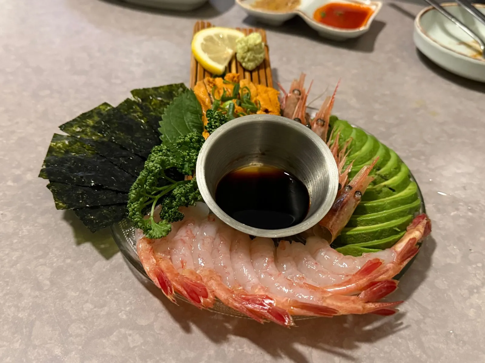 A plate with shrimp, avocado, and seaweed arranged around a small bowl of soy sauce