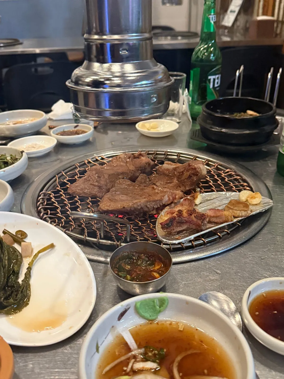 숯불 위 석쇠에 올린 고기와 그 둘레의 반찬 그릇