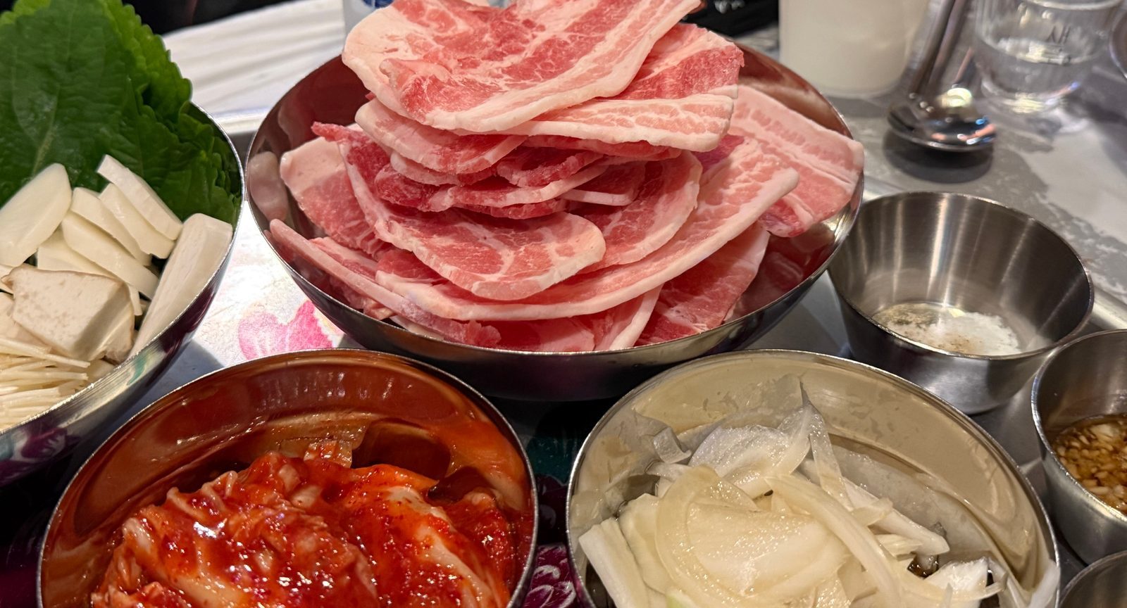 Thin frozen pork belly stacked in a steel bowl, with kimchi and rice cakes