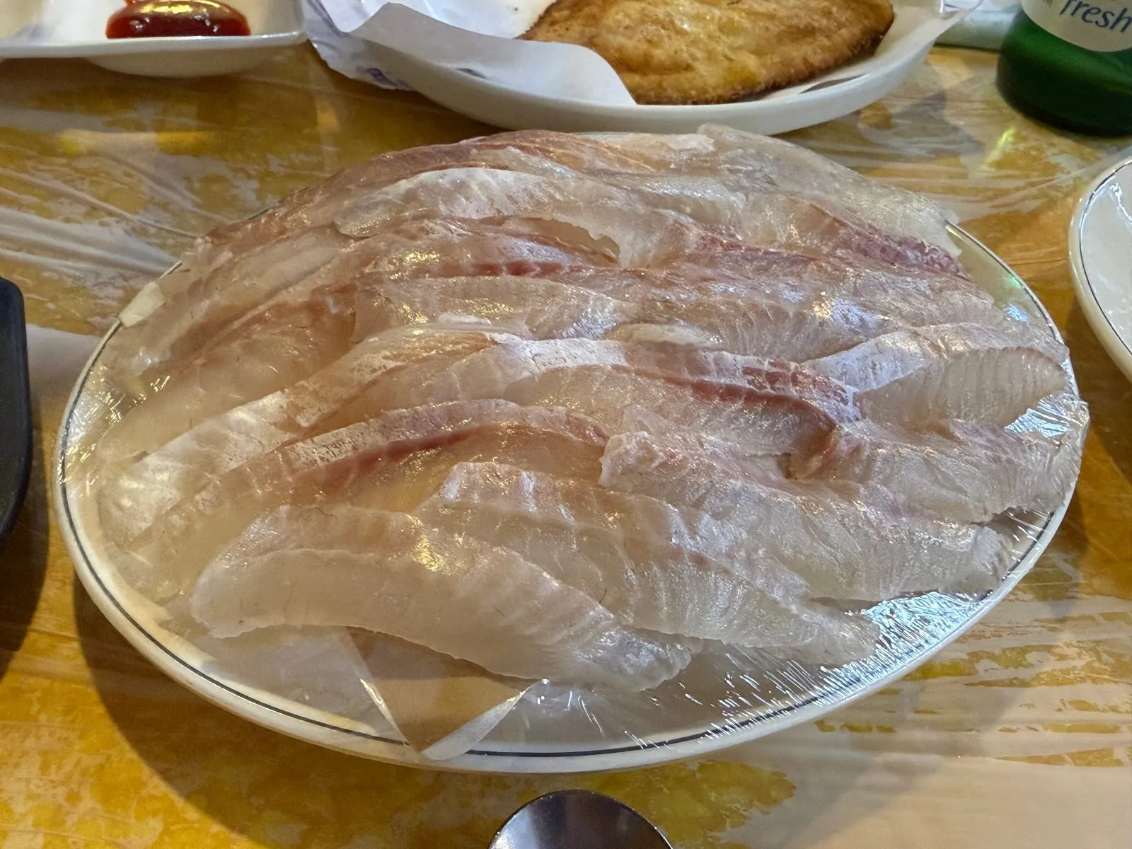 Thin slices of white fish laid out neatly on a wide plate