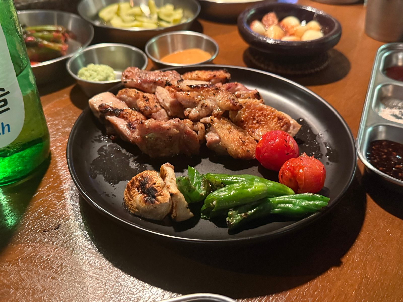 검은 접시에 담긴 닭 모듬구이와 꽈리고추, 방울토마토, 마늘