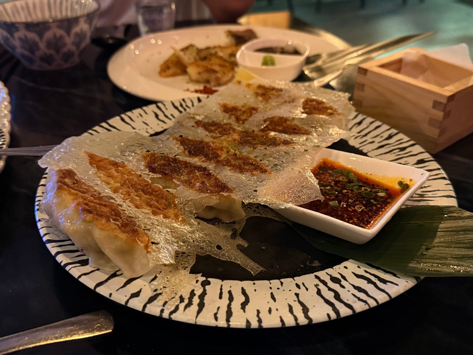 Pan-fried gyoza lined up on a patterned plate with dipping sauce