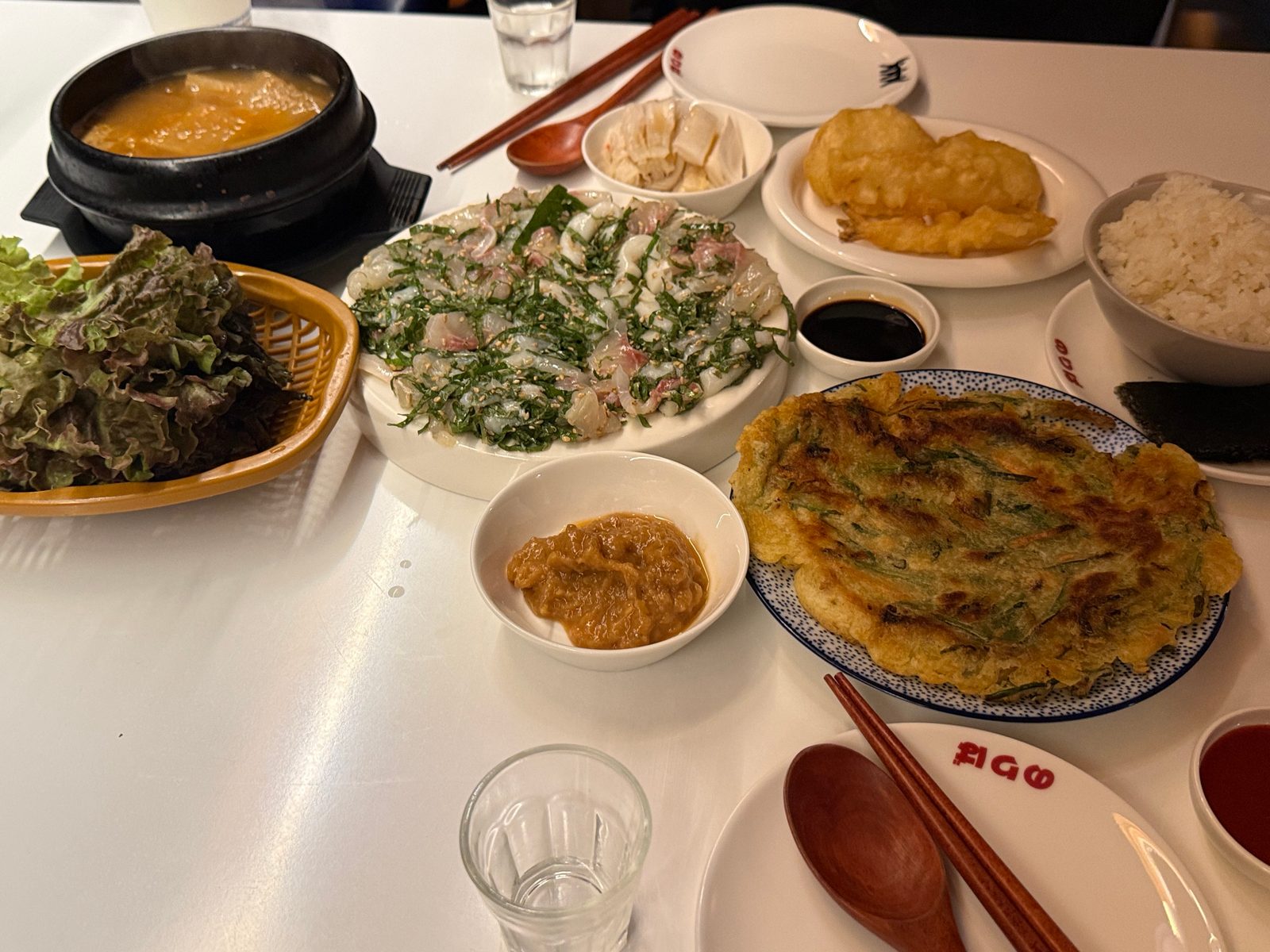 Raw fish with perilla, a pancake, leaves for wrapping, and a stew on a white table