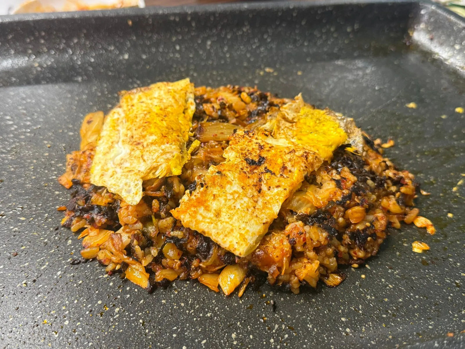 Kimchi fried rice on a grill plate, topped with two wide pieces of egg and seaweed