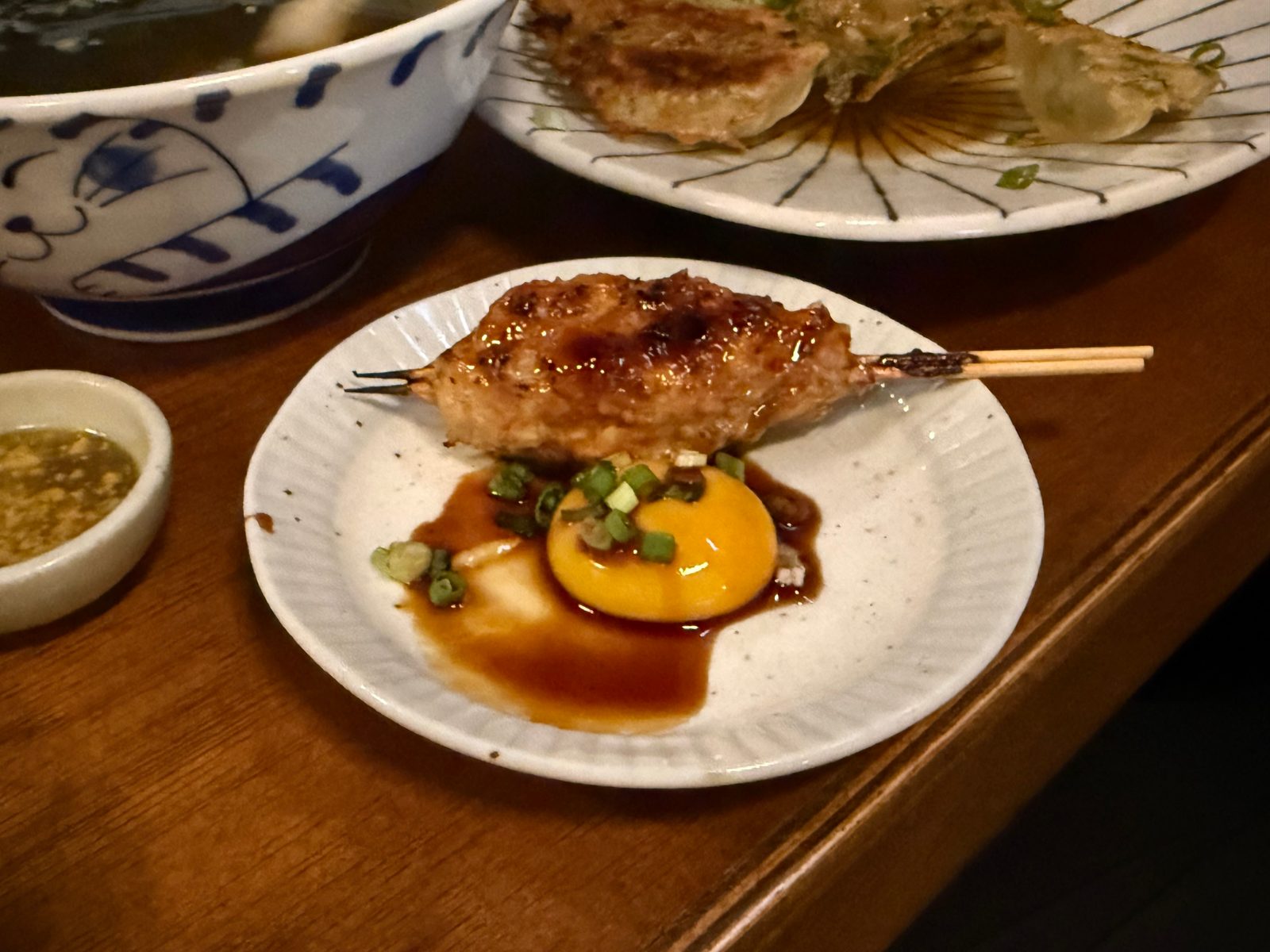 A tsukune skewer on a white plate with an egg yolk sauce in front