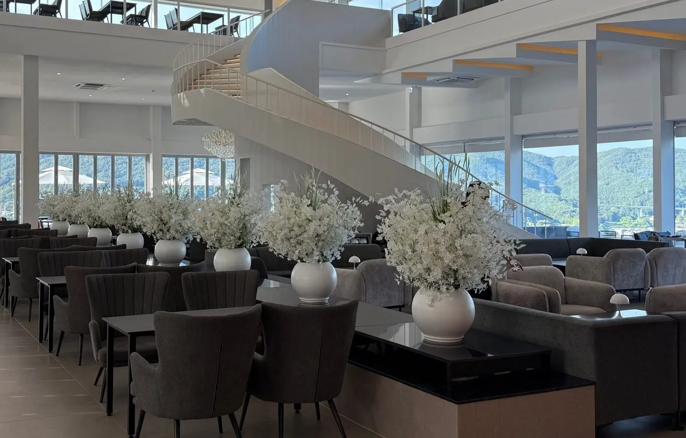 A large interior with a white staircase, flower decorations, and rows of tables