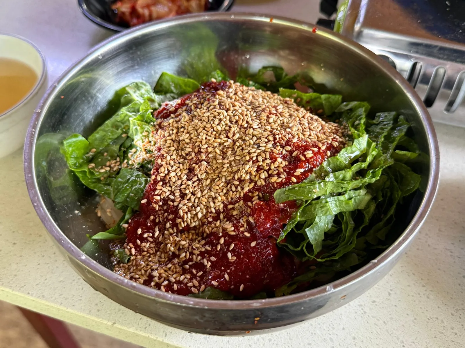 Bibim-guksu in a steel bowl topped with lettuce, red sauce, and sesame