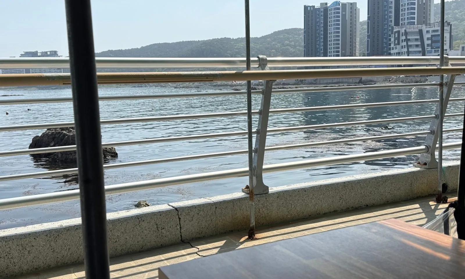 난간 너머로 보이는 잔잔한 바다와 멀리 있는 건물